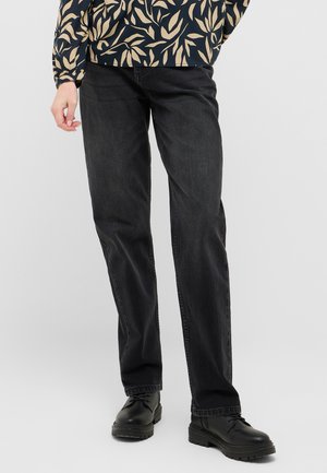 Schwarze Denim-Jeans mit geradem Schnitt, die über eine subtile Textur und kontrastierende Nähte verfügen, kombiniert mit schwarzen Schnürstiefeln.