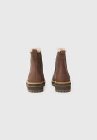 Botas de tobillo de cuero marrón con cuello de piel de oveja, paneles laterales elásticos y suelas texturizadas. Presenta detalles de costura y un tacón bajo tipo bloque.