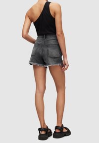 Top negro de canalé con un tirante, combinado con pantalones cortos de mezclilla grises de cintura alta con bordes deshilachados y dos bolsillos traseros. Sandalias negras.