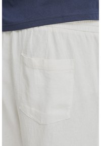 Světlá, texturovaná látka s náprsní kapsou. Horní část oděvu je tmavě modrá, viditelná podél horního okraje.