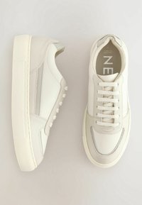 Baskets en cuir blanc avec des accents texturés, un panneau latéral surélevé, des lacets plats et un col rembourré. Semelle en caoutchouc avec un design léger et épuré.