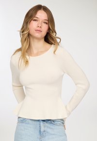 Top a maniche lunghe color crema con coste, corpo aderente e orlo a peplo, realizzato in tessuto a maglia strutturato, abbinato a denim azzurro chiaro.