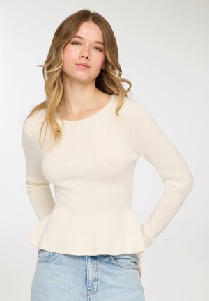 Top a maniche lunghe color crema con coste, corpo aderente e orlo a peplo, realizzato in tessuto a maglia strutturato, abbinato a denim azzurro chiaro.