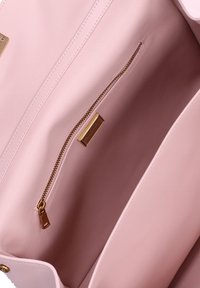 Interno di una borsa in finta pelle rosa chiaro con una tasca con zip. Presenta una texture liscia, una cerniera color oro e un'etichetta del marchio.