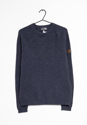 Sweat-shirt bleu foncé en maille côtelée à manches longues suspendu sur un cintre noir, avec un écusson en cuir rond sur le coude gauche.