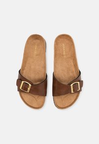 Brune sklidesandaler med en bred rem og gullspenne, med en teksturert fotbeholder og flat såle. Merkenavnet preget i gull.