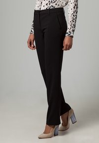 Mustat räätälöidyt housut suorilla lahkeilla. Yhdistetty kuvioituun puseroon ja beigenvärisiin korkokenkiin, joissa on teksturoidut, läpinäkyvät paksut korot.