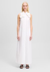 Robe maxi sans manches blanche avec un devant à boutons et un col à accents floraux. Tissu lisse, coupe droite et design longueur cheville.