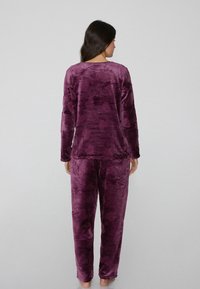 Conjunto de pijama morado de felpa, confeccionado en un material suave y aterciopelado. Parte superior de manga larga y pantalones con un ajuste holgado. Textura lisa con patrones sutiles.