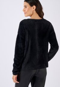 Schwarzer, flauschiger Pullover mit lässiger Passform, überschnittenen Schultern und langen Ärmeln. Sanfte Textur mit einem einfachen, minimalistischen Design.
