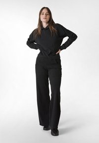 Svart långärmad hoodie med lös passform och huva, tillsammans med vida svarta byxor. Mjuk tyg med minimal detaljering.