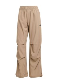 Beżowe spodnie sportowe wykonane z gładkiej tkaniny, wyposażone w elastyczny pas, detal z logo oraz zamki na dole nogawek umożliwiające regulację.