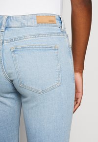 Vaaleansiniset farkut, joissa on nahkaleima vyötäröllä ja takataskussa timantin muotoinen yksityiskohta. Sujuva pinta ja näkyvät saumat.