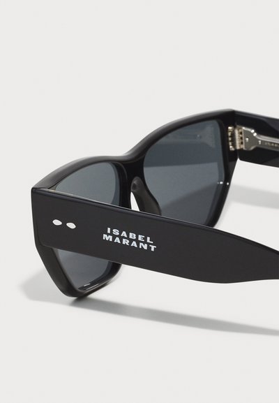 Lunettes de soleil noires rectangulaires avec des verres gris, large monture en plastique et logo "ISABEL MARANT" blanc sur le côté. Design angulaire, finition brillante.