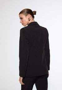 Black tailored blazer with a smooth texture, structured lapels, and a fitted design, shown from the back with minimal detailing.