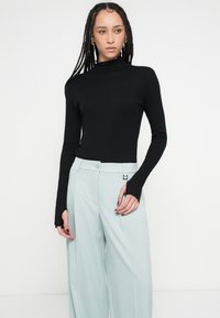 Fekete garbó hosszú ujjú felső, világoskék bő szárú nadrággal párosítva; hüvelykujj kivágásokkal és sima, rugalmas anyagból.