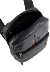 Schwarze Leder-Crossbody-Tasche mit verstellbarem Tragegurt, zwei Reißverschlussfächern und einer strukturierten Oberfläche mit Logo-Akzent.