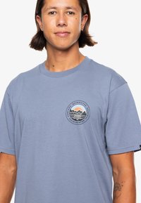 Light blue, short-sleeve t-shirt with a round logo featuring mountains and sun. Made of soft fabric, with a relaxed fit.
