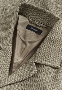 Sacou în carouri houndstooth maro, cu guler croit, captuseală bej deschis moale și etichetă cu inscripția „Matinique”. Dispune de reveruri structurate și țesătură texturată.