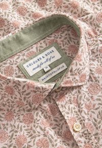 Camicia a fantasia floreale in morbido tessuto rosa chiaro con colletto verde. Presenta etichette che indicano marca e taglia, con bottoni color crema sul davanti.
