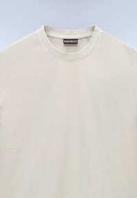 T-shirt beige chiaro a maniche corte con scollatura tonda, realizzato in morbido tessuto di cotone, caratterizzato da una superficie liscia e un design minimale.