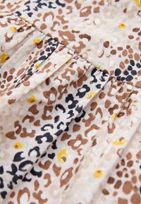 Gaisīga auduma ar bēša fonu, kam raksturīgas brūnu, melnu un dzeltenu leoparda plankumu kombinācijas un mazi ziedu detaļas. Savākta tekstūra.