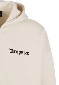 Sweat à capuche beige avec une capuche affichant un texte gothique noir "Dropsize" brodé sur la poitrine.