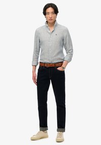 Lichtblauwe gestreepte overhemd met knopen, donkere spijkerbroek, bruine riem en beige sneakers. Het shirt heeft een kraag en opgerolde mouwen.