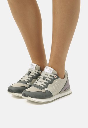 Zapatillas grises y beige con parte superior texturizada, cordones y un pequeño acento morado en el talón. Presentan un logo y detalles reflectantes.