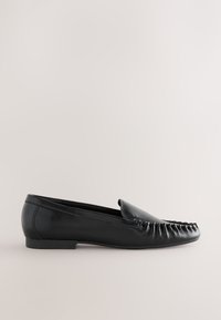 Chaussure plate style mocassin en cuir noir avec des détails cousus sur l'embout arrondi et un talon bas, vue de profil sur un fond neutre.