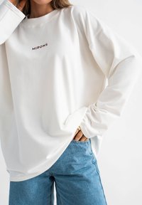 Wit sweatshirt met lange mouwen, een geribde ronde hals en geborduurde tekst "MIRONS." Gecombineerd met lichtblauwe spijkerbroek. Zachte, casual stof.