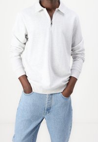 Sudadera de cremallera gris claro con cuello y mangas largas, hecha de una mezcla de algodón. Combinada con jeans de mezclilla azul claro.
