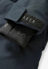 Mantil s dugim rukavima u mornarskoj boji s mekanom teksturom, crna čičak oznaka s natpisom "BAKER" i kontrastna crna elastična traka s utisnutim slovima.