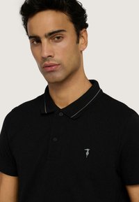 Czarna koszulka polo wykonana z bawełny, z kontrastowym kołnierzykiem, trzyguzikowym zapięciem oraz małym haftowanym logo na klatce piersiowej.