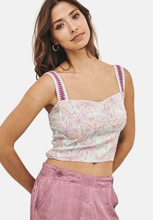 Top corto verde claro con un patrón de palmeras, escote cuadrado y tirantes anchos con detalles en rosa. Combinado con pantalones de talle alto texturizados en rosa.