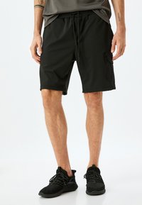 Sorte atletiske shorts med elastisk talje og snøre, med en sidelomme og glat, letvægts stof.