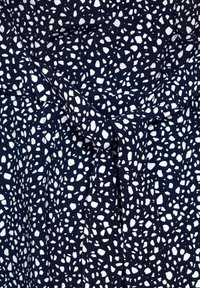 Tessuto da abito blu navy con un motivo a ciottoli bianchi, caratterizzato da un dettaglio con fiocco frontale e pieghe per texture e forma.