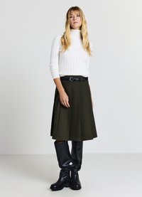 Pull blanc à col roulé côtelé, jupe plissée olive avec une ceinture noire, et bottes en cuir noires montantes jusqu'aux genoux. Silhouette simple et structurée.