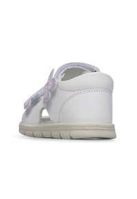 Sandal de cuero blanco con tacón bajo, que presenta acentos de mariposa, recortes laterales y una suela de goma texturizada para agarre y comodidad.