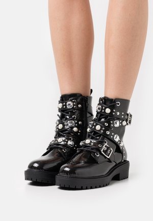 Bottes bottines en cuir verni noir avec plusieurs sangles, boucles argentées, perles décoratives et strass. Semelle en caoutchouc épaisse.