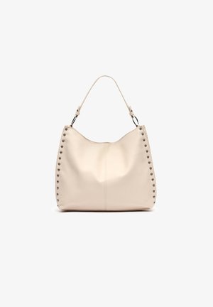 Borsa a mano in pelle beige con forma curvata, dettagli borchiati lungo il lato e una sola tracolla regolabile. Texture liscia, design minimale.