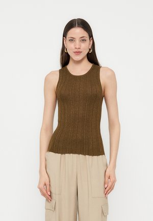 Femme portant un haut sans manches côtelé marron et un pantalon cargo beige, debout avec les bras détendus devant un fond blanc uni.