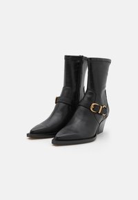 Botas de cuero negro hasta el tobillo con punta afilada, cierre con cremallera, acento de correas trenzadas y tacón de cuña. Textura suave y diseño elegante.