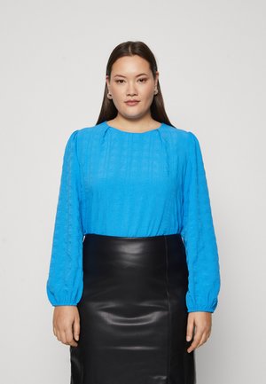 Blue textured long-sleeve top with a round neckline, paired with a black sleek leather skirt, displayed against a neutral background.