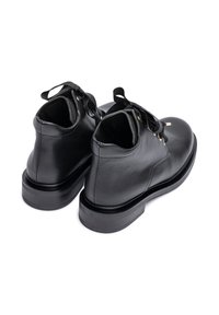 Pair of black leather ankle boots with black ribbon laces, gold eyelets, and thick black rubber soles shown from the back and side.