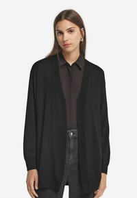 Svart cardigan i mjukt stickat tyg, öppen frontdesign med långa ärmar, med lös passform och ribbade muddärmar.