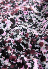 Tissu avec un motif abstrait de points irréguliers éparpillés en noir, blanc, rose et bordeaux sur un fond sombre, présentant des plis doux.