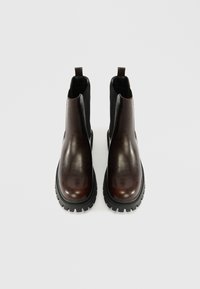 Καφέ δερμάτινες μποτίνες Chelsea με ελαστικές πλευρικές πάντες, στρογγυλή μύτη και υφή μαύρης καουτσούκ σόλας. Διαθέτουν θηλίτσα για εύκολη φόρεση.