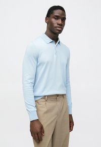 Gaiši zila garām piedurknēm polos krekls ar apkakli un divu pogu aizdari, kopā ar bēša krāsas piegrieztām biksēm. Gluda tekstūra, pieguļošs dizains.