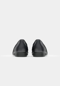 Paire de chaussures habillées en cuir noir vue de dos sur un fond gris clair uni.